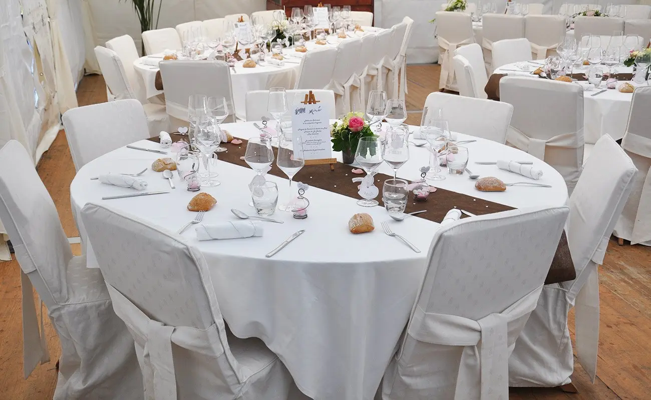 Tables rondes dressées et chaises en teck habillées de housses blanches