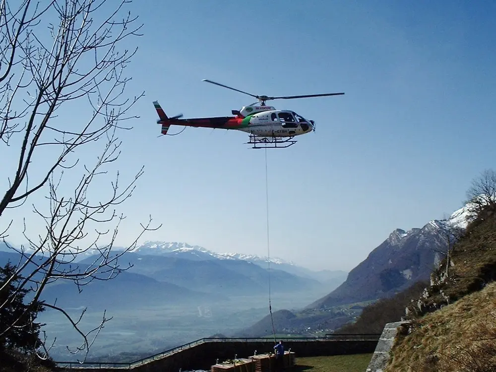 Hélicoptère transportant du matériel de tente au-dessus de la vallée, depuis le Fort de Tamié