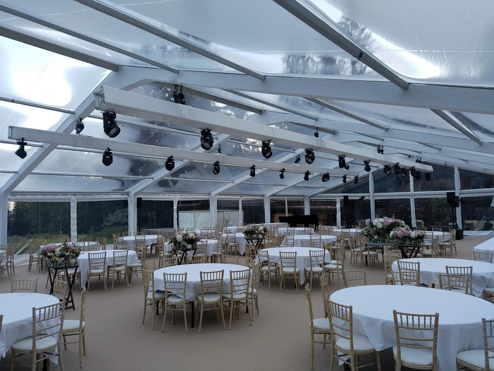 Intérieur d’une tente transparente dressée de tables rondes nappées et de chaises dorées