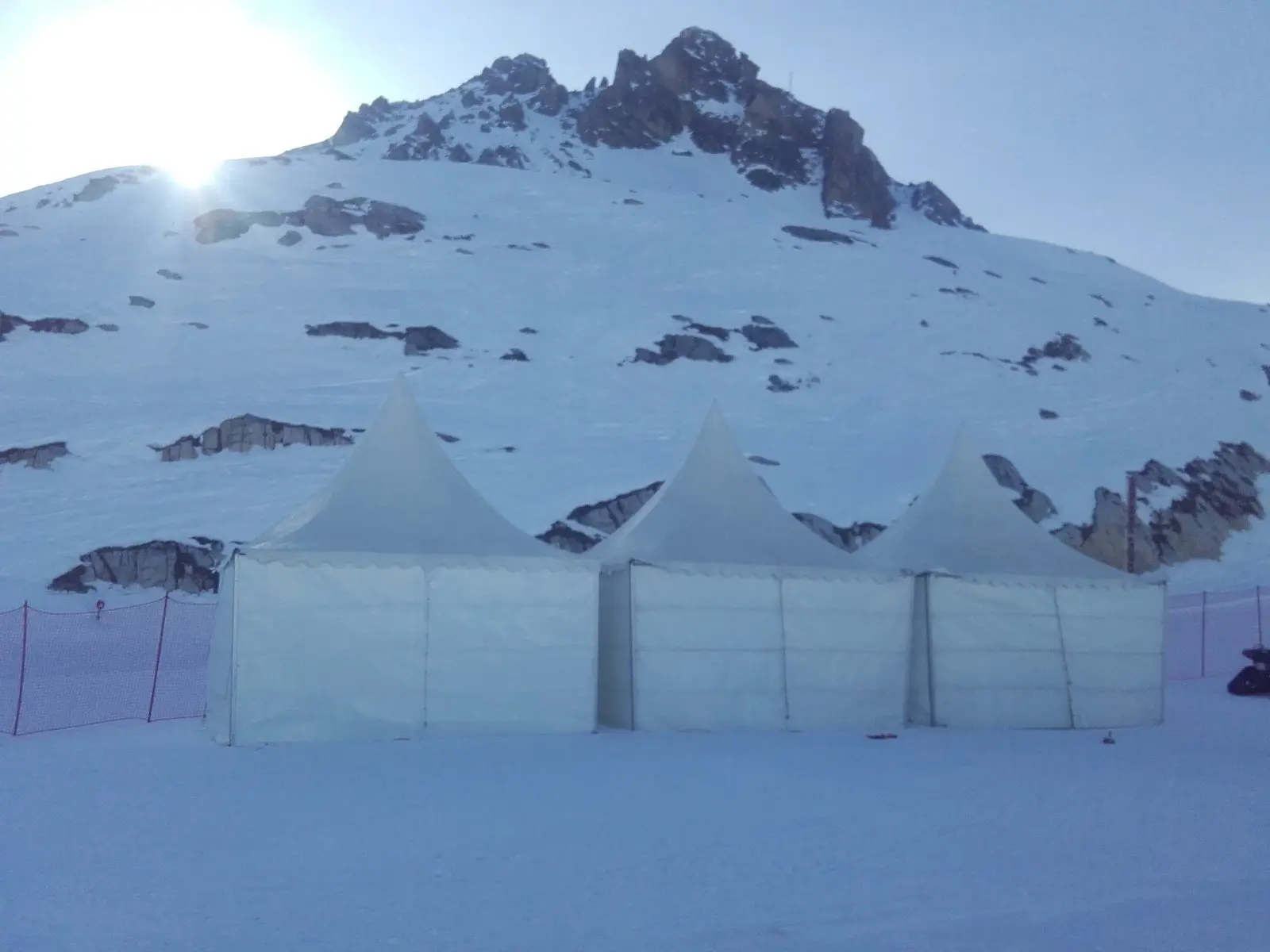 Trois tentes à pointe montées sur la neige au pied d’un sommet rocheux, à Val d’Isère